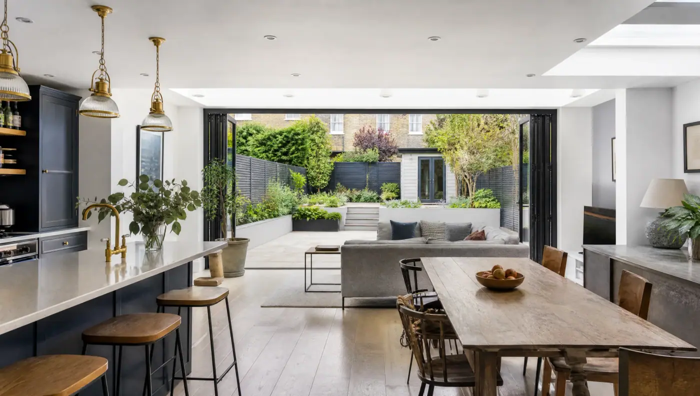 Open-plan kitchen, dining and living space with a long oak table and folding glass doors onto a landscaped garden