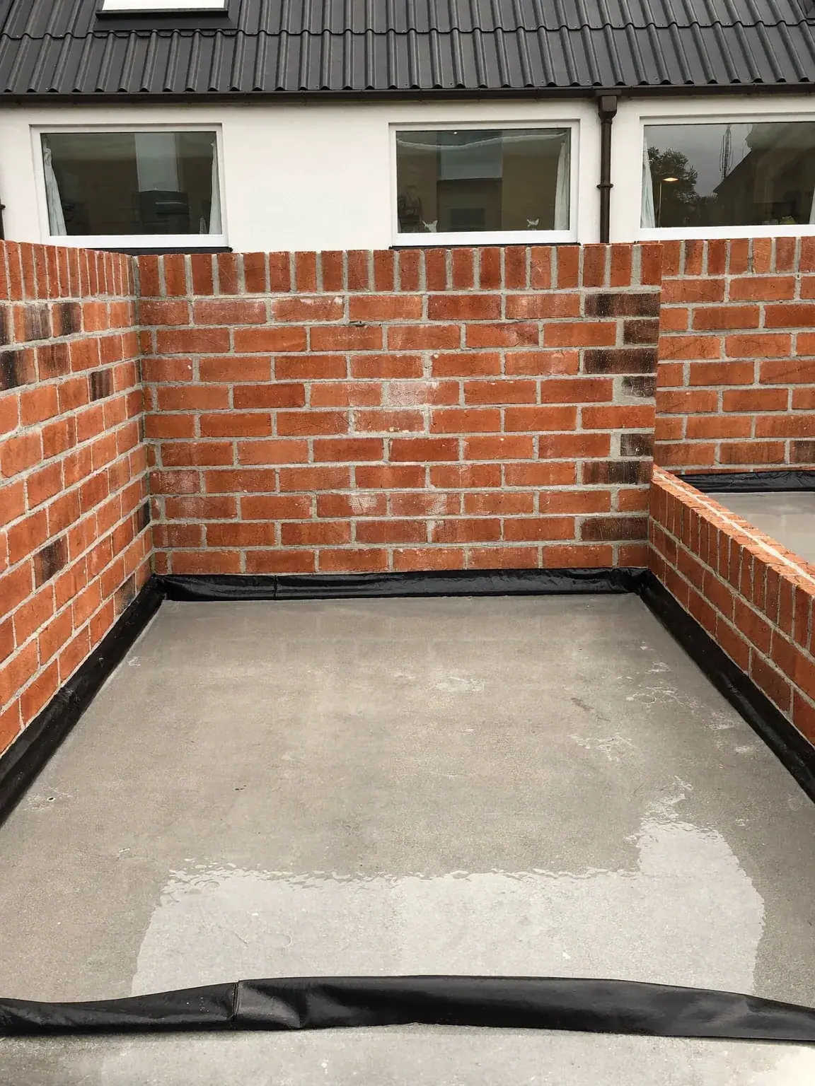 Freshly poured concrete floor slab with a black damp-proof membrane turned up against new brick walls
