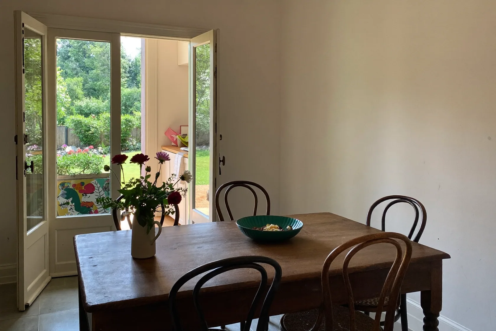 Dining table with bentwood chairs beside open French doors onto a garden